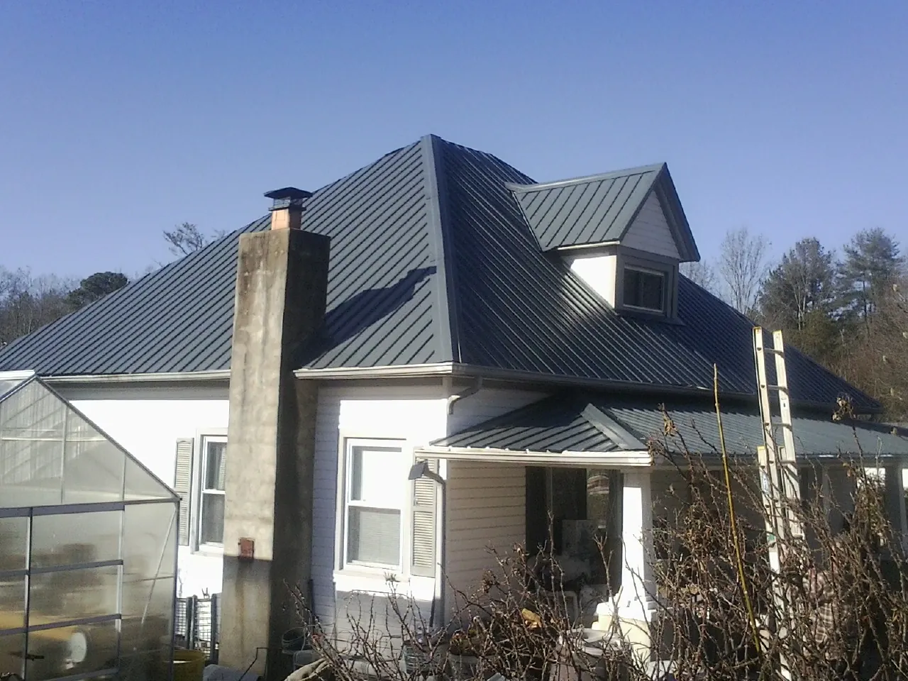Dark blue standing seam metal roof on a white farmhouse with dormer — Slate & Tile Roof Repair by Roofing Brothers in Armonk