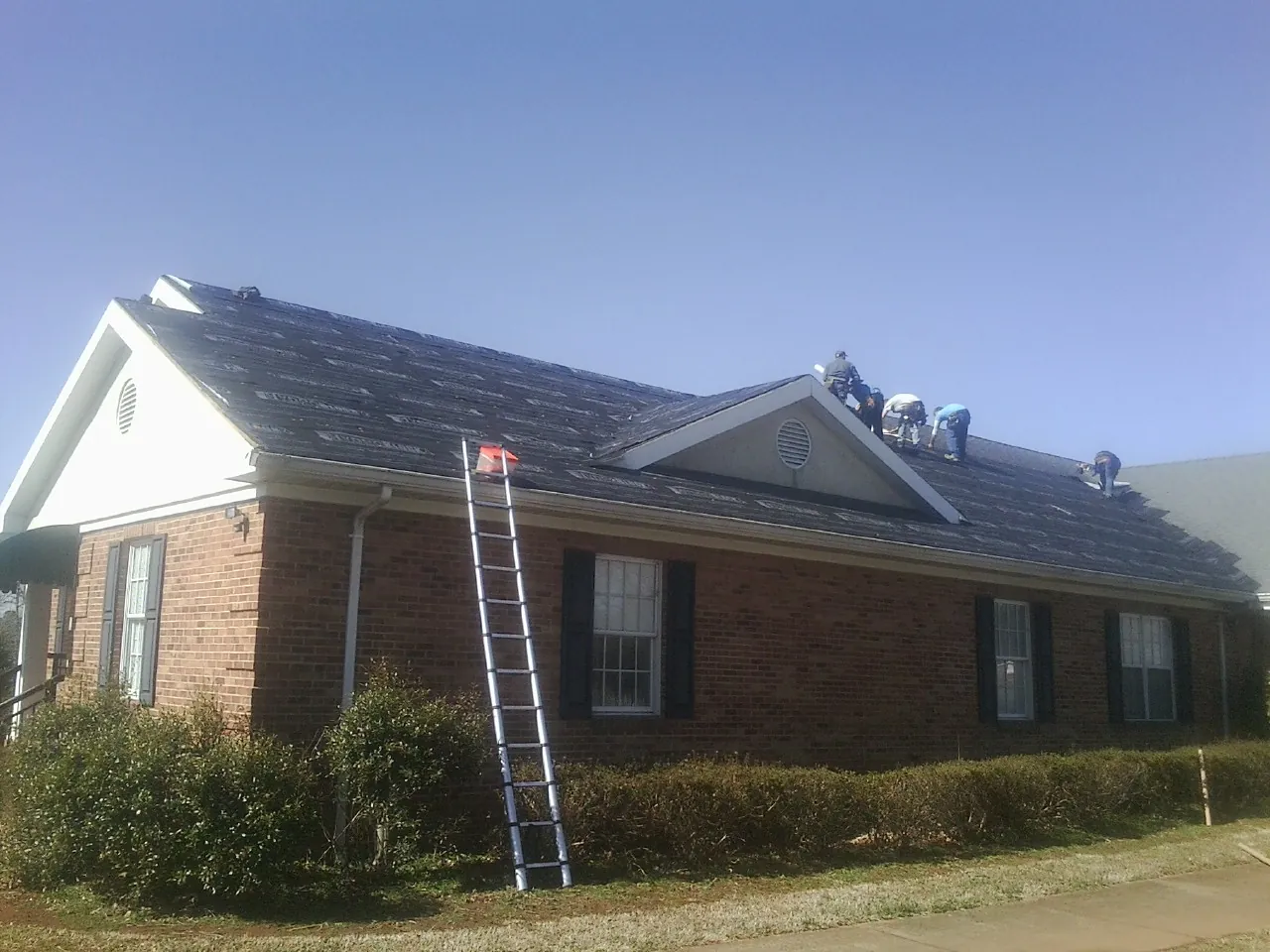 Crew tearing shingles off a brick ranch roof with a ladder set — Emergency Roof Repair work by our crew in Armonk