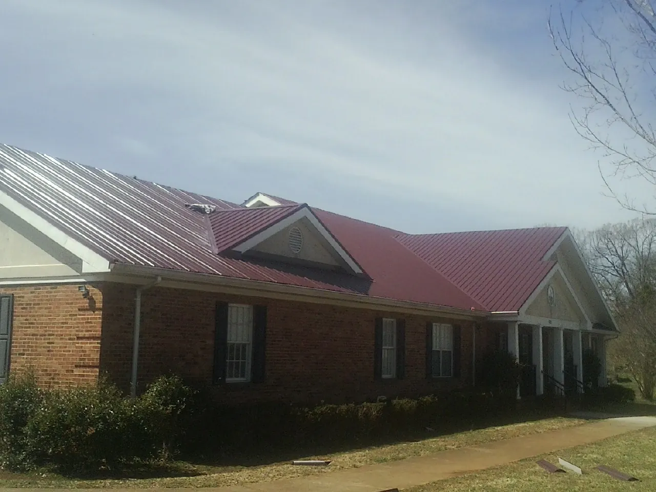 Red metal roof with gabled entries on a long brick building, from a Hail Damage Roof Repair job in Armonk