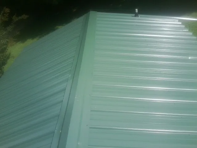 New green metal panels meeting at the ridge of a roof — Flat Roof Repair work by our crew in Armonk