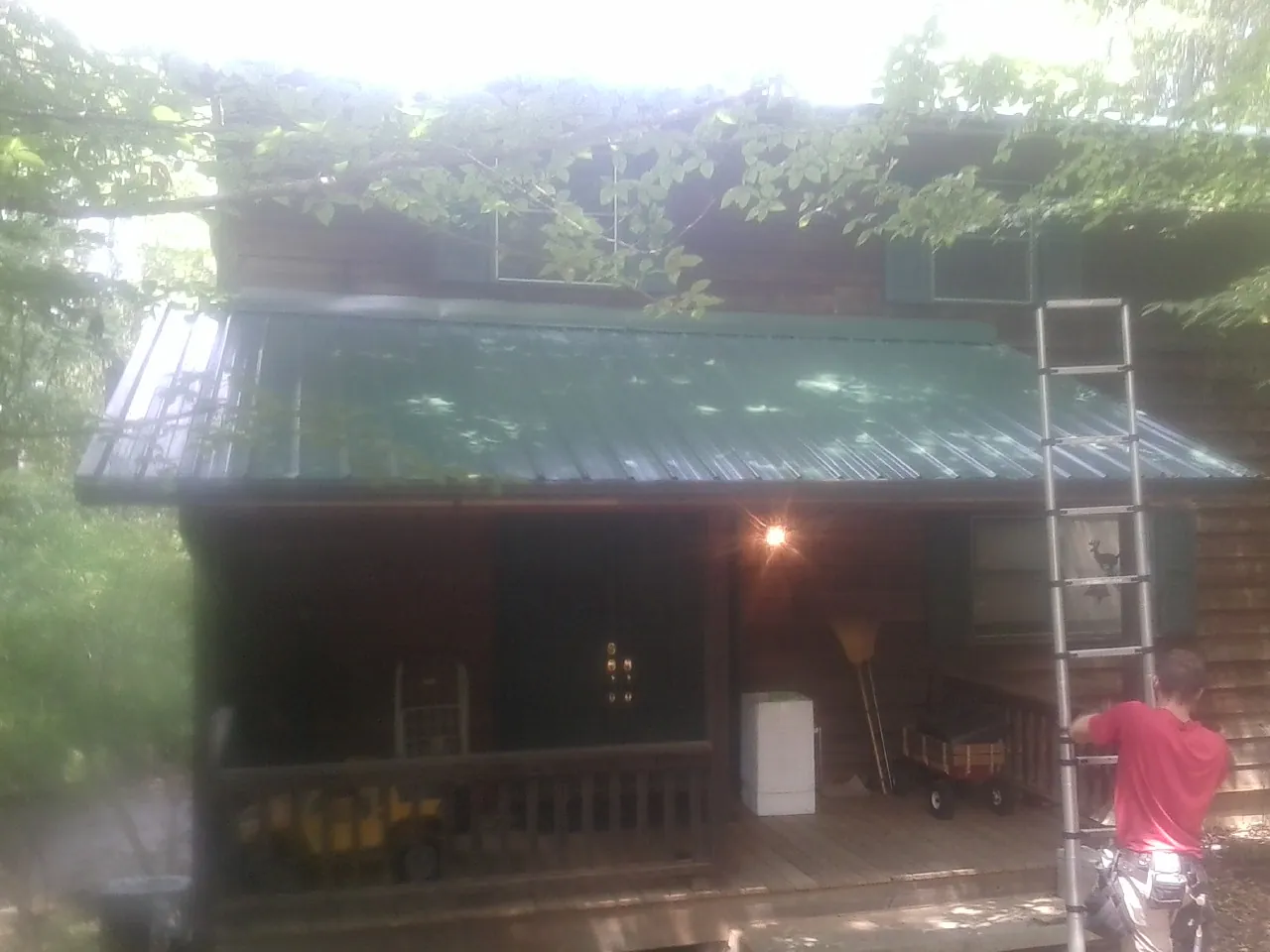 Worker on a ladder at the green porch roof of a wooded cabin in Armonk