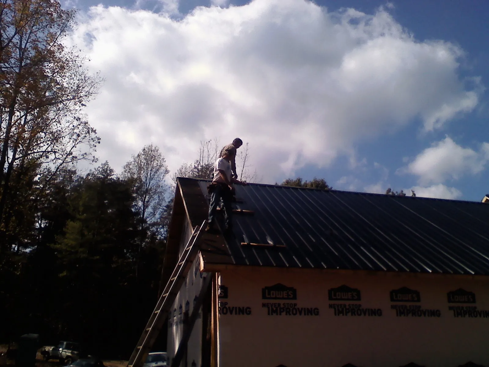 Roofer fastening dark metal panels high against a cloudy sky, from a Roof Inspection job in Armonk